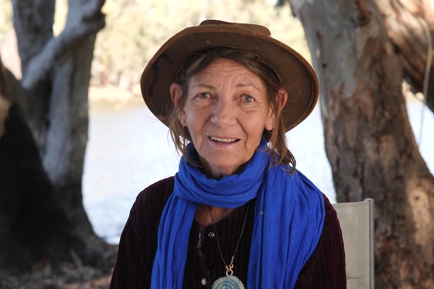 A woman wearing a hat is staring at a camera with a blue scarfe on 