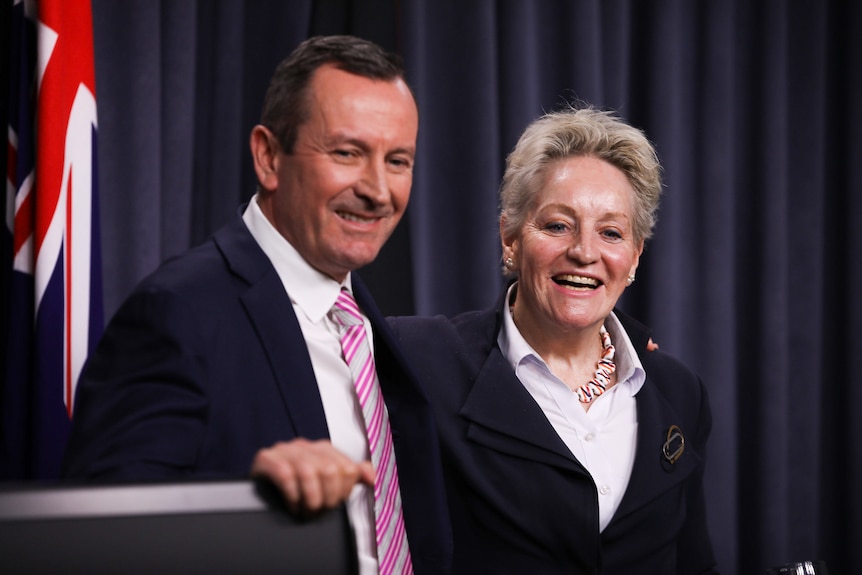 A man and a woman stand next to each other, both with warm smiles.