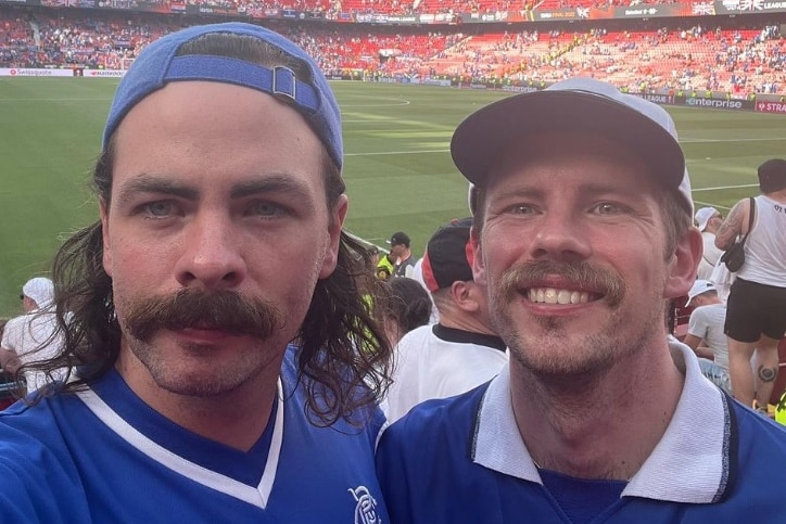 Chris Ross smiles next to a friend inside a football stadium