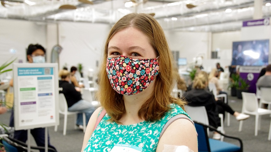 A woman wearing a mask and a sleeveless top sits in a vaccination hub.