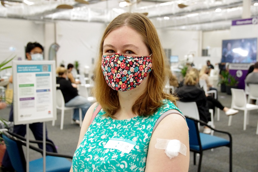 A woman wearing a mask and a sleeveless top sits in a vaccination hub.