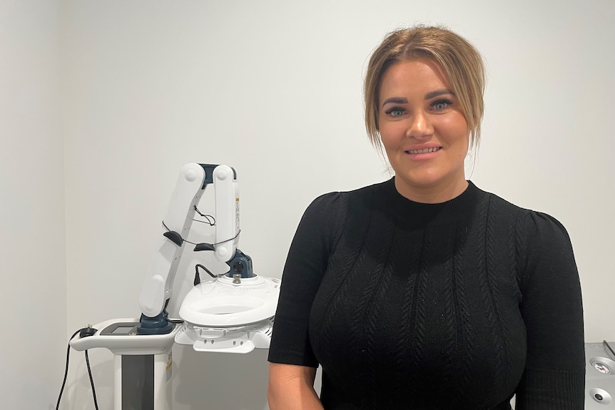 Woman in black t-shirt, smiling, standing in front of lab type equipment