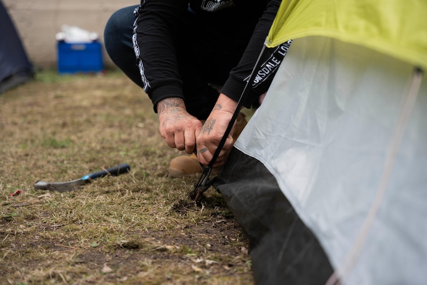 Man sits next to a tent fixing a seam. 