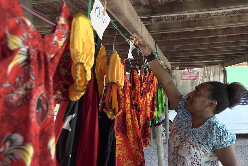 Seamstress Dulcie Maliaki hangs vibrantly coloured clothes she's made on a line.