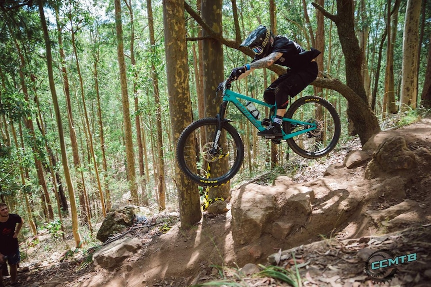 A rider wearing black on a black bike does a gap jump between two rocks.