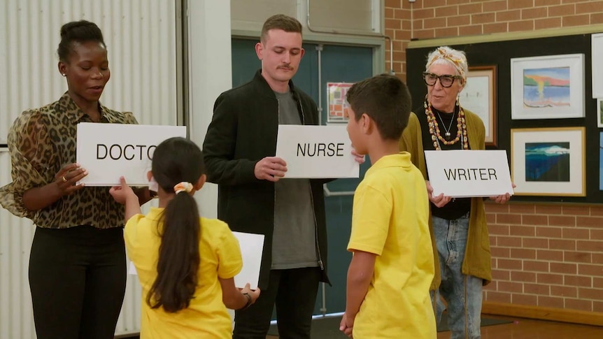Three adults each holding different signs, "doctor" "nurse" "writer" with two school kids