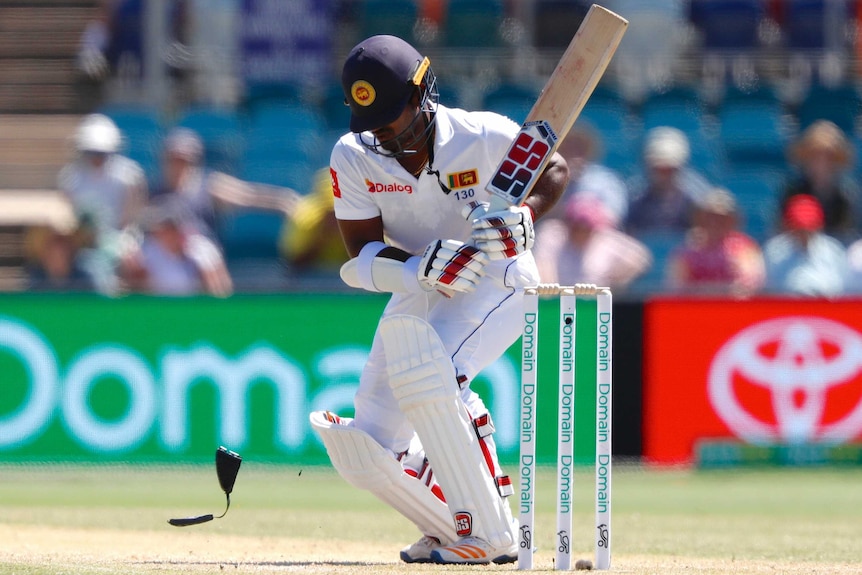 Kusal Perera crouches after he is hit on the helmet by a bouncer as his neck guard bounces to the turf