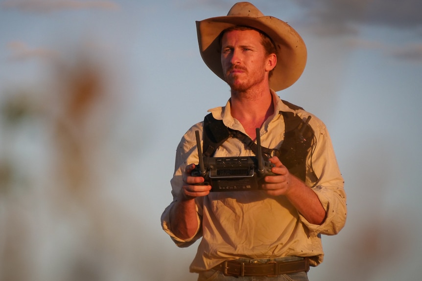 Young cattle grazier holding remote control looking out to horizon 