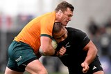 A Wallabies player holds the ball as he collides with an All Blacks opponent.