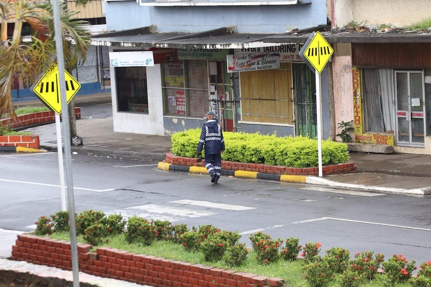 A man in a police uniform walks across an empty street.