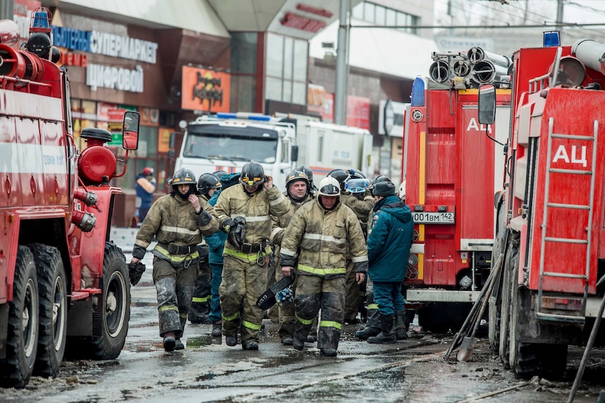 A group of firefighters walk past their fire trucks near the scene of the multi-storey shopping centre fire in Russia.