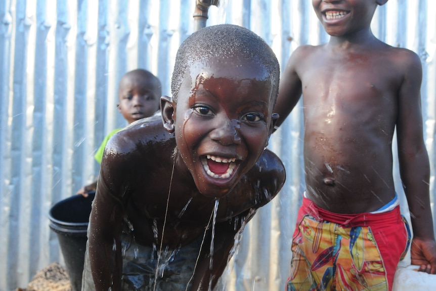 child with water over his head, smiley, cute, african child 