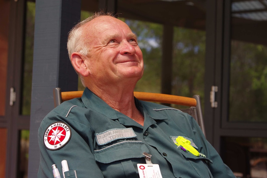 Man in volunteer ambulance uniform sitting on chair looking up smiling