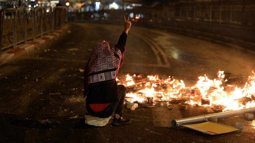 A Palestinian sitting next to a burning barricade flashes a ''V'' sign during clashes with Israeli police.