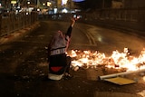 A Palestinian sitting next to a burning barricade flashes a ''V'' sign during clashes with Israeli police.