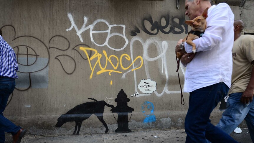 People walk by street art graffiti in New York by Banksy
