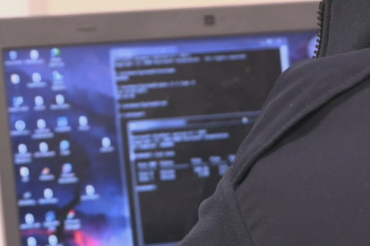 Hombre en capucha en computadora con pantalla borrosa en el fondo