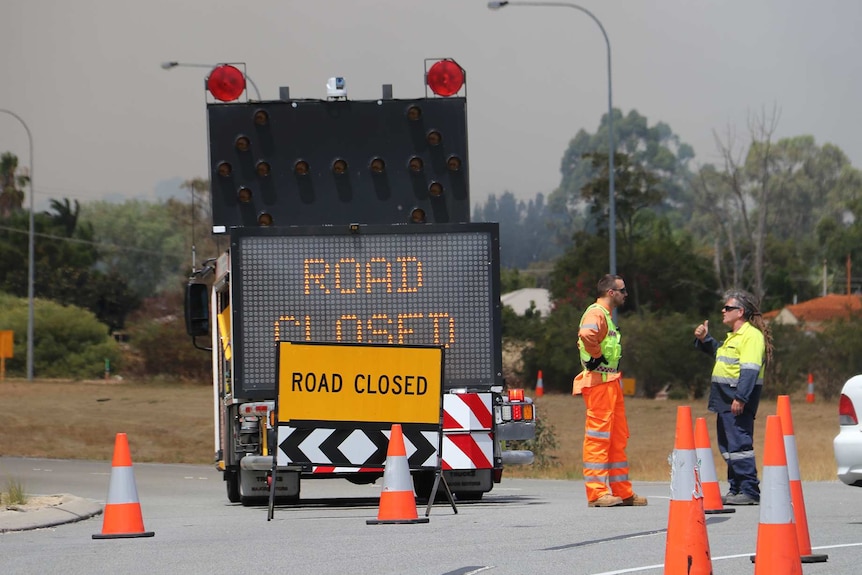 Firefighters stand next to a road closed sign.