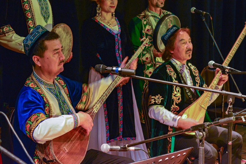 Two men in traditional Uyghur hats and dress hold long-necked lutes.