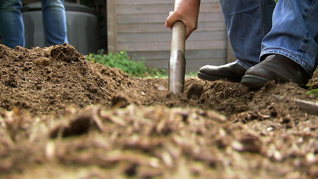 Person digging soil with a spade.