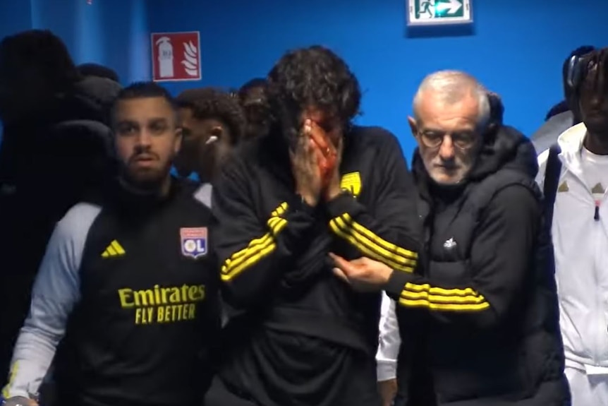 Olympique Lyonnais coach Fabio Grosso is led down a hallway, holding his face in his hands.