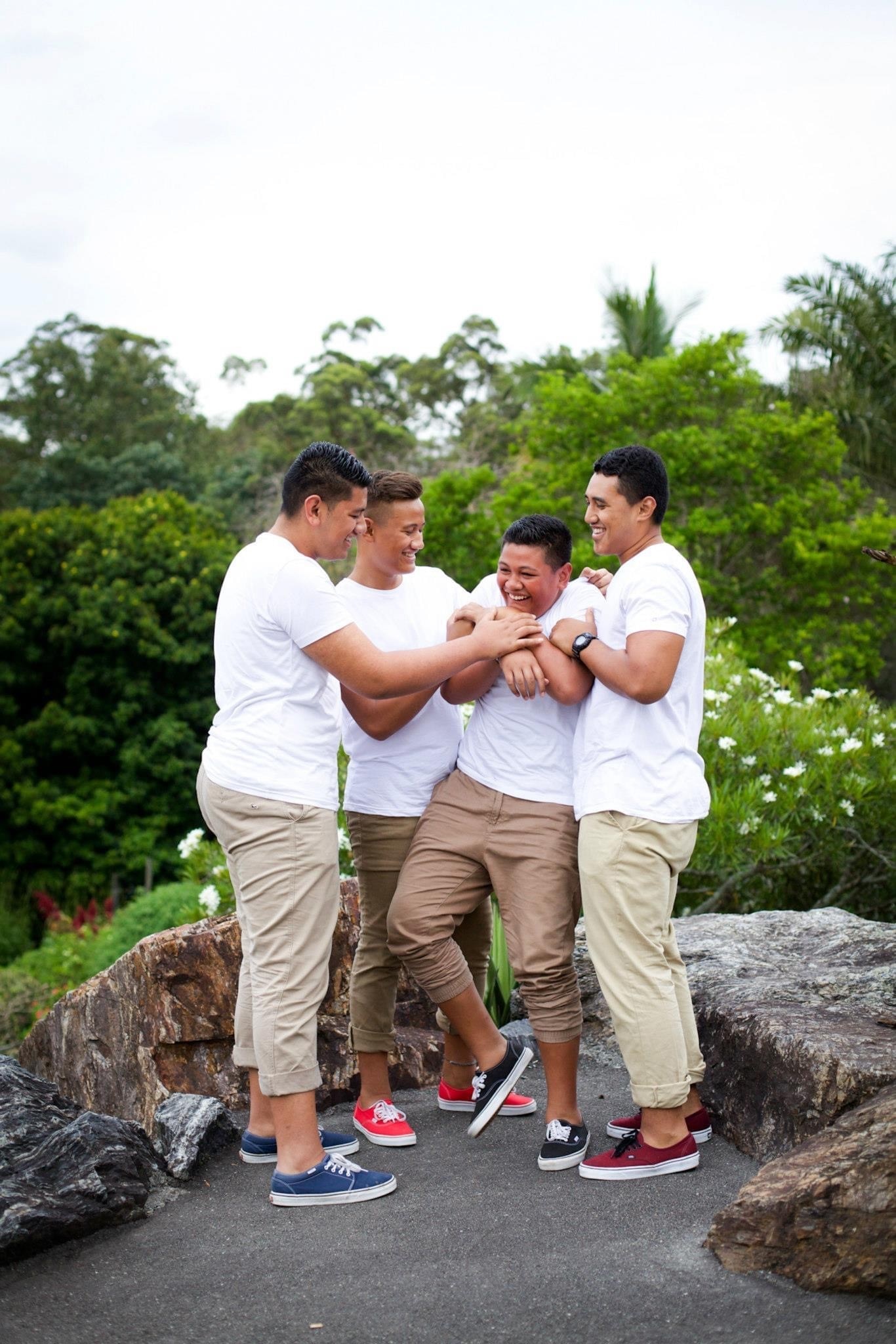 Four young men in white t-shirts with their arms around each other.