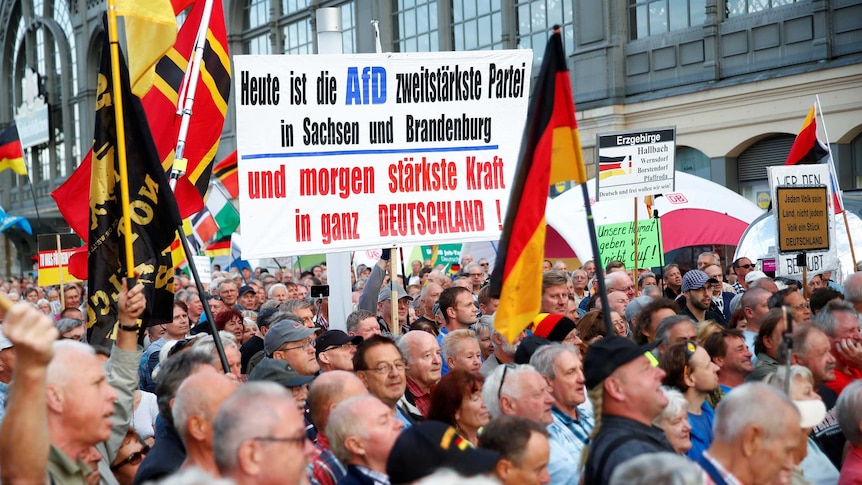 Hundreds of people rally down a street holding up signs and flags