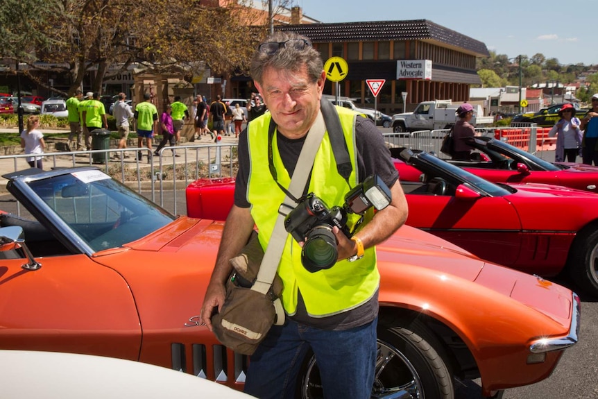 A man in high visibility vest holding a camera in front of race cars in Bathurst, NSW