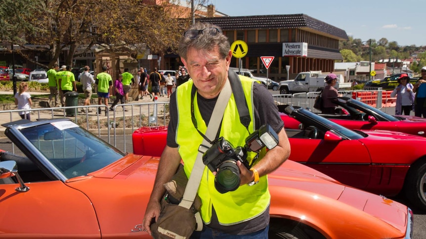 A man in high visibility vest holding a camera in front of race cars in Bathurst, NSW