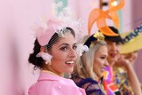 A woman with a pink fascinator smiles to camera with her three friends in the background.