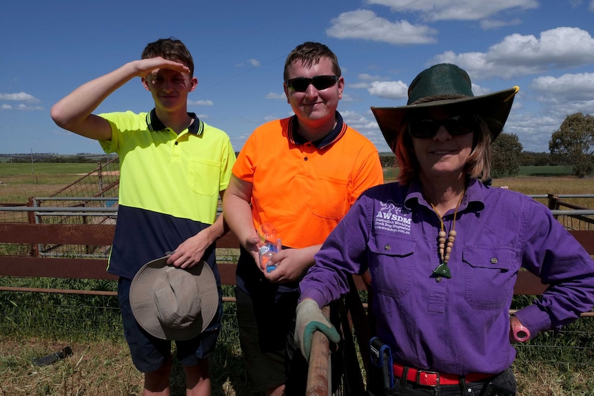 Two youn g men wearing hi viz stand with an older woman in a hat.