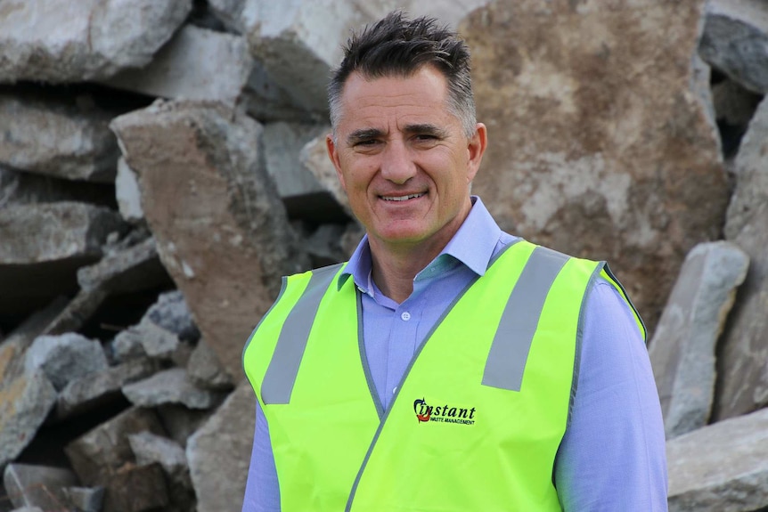 Mid shot of a man wearing a fluoro jacket at a waste recycling facility.