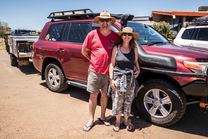 Two people stand beside their car wearing sunhats