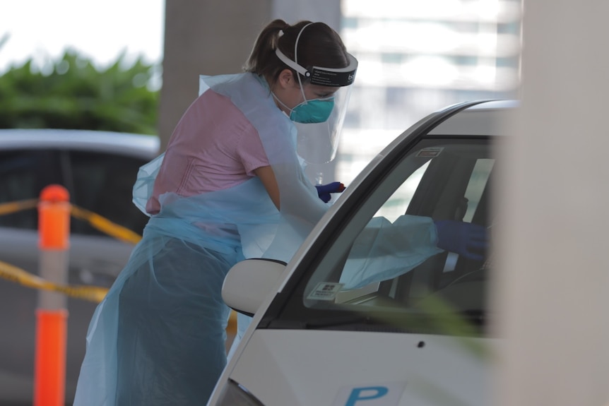 Woman in personal protective gear leans into a car window