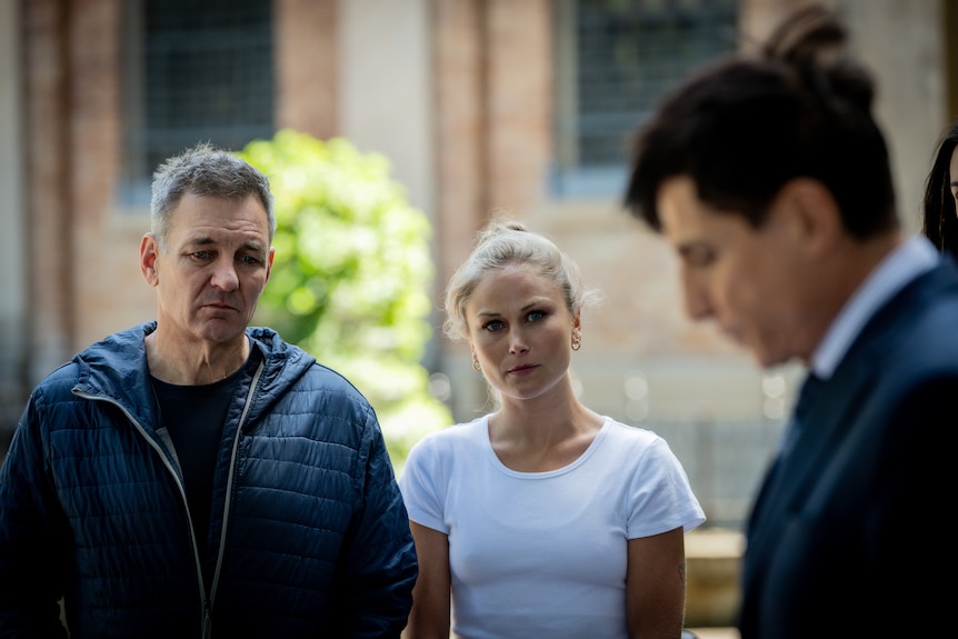 Matt Barker and Grace Tame watch another man speak at a press conference