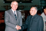 A man in a western suit grins as he shakes the hand of a man in a Mao suit
