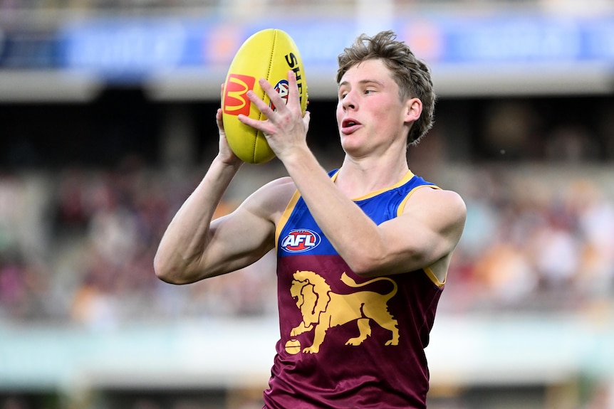 jaspa fletcher holds the ball in front of his face while playing the saints at the gabba