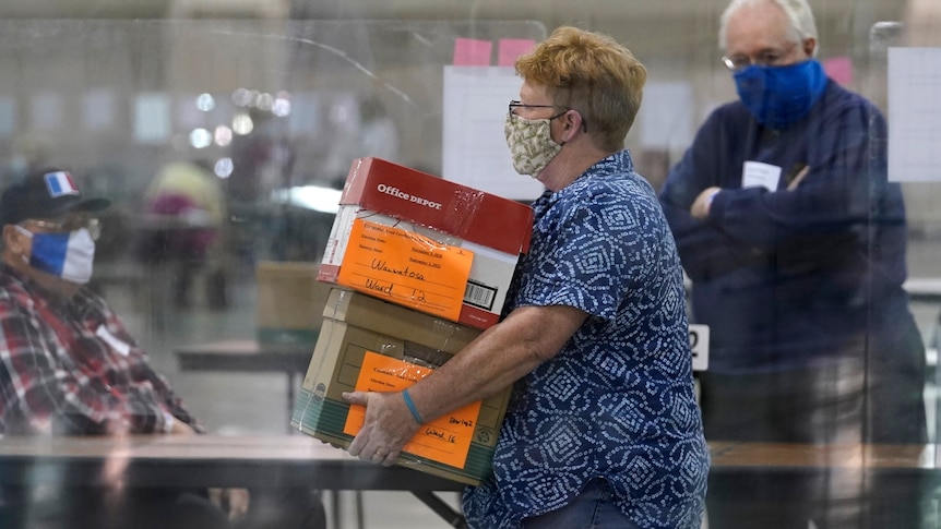 An election official wearing a mask walks with boxes full of ballots at the Wisconsin Center in Milwaukee