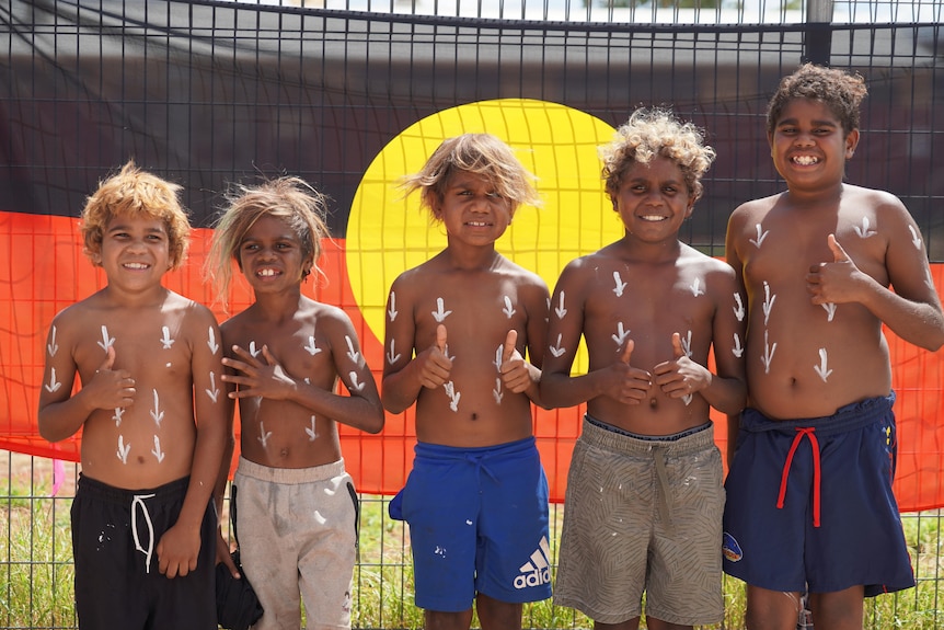 Children stand in front of the Aboriginal flag