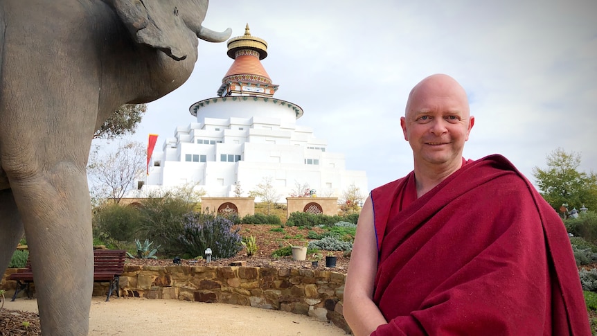 a Buddhist monk smiles at the camera in front of a temple