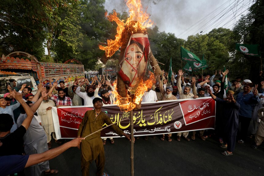 A group of men surround a burning picture of Nupur Sharma on a stick. 