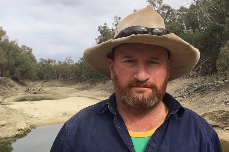 Man with a hat stands in front of a small puddle of water on the Lower Darling.