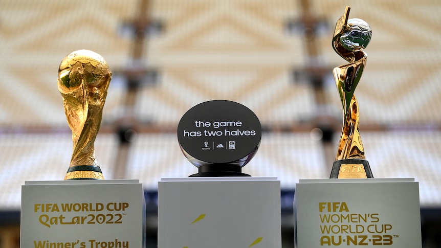 The trophies for the men's and women's FIFA World Cup on plinths with a sign reading "It's a game of two halves" between them.