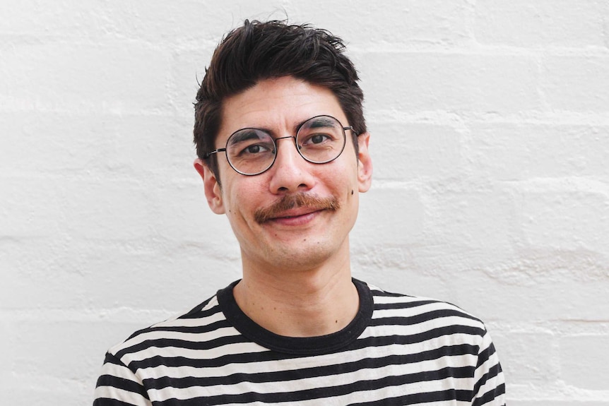 A man with a moustache and glasses wearing a black and white horizontally striped t-shirt smiling at the camera