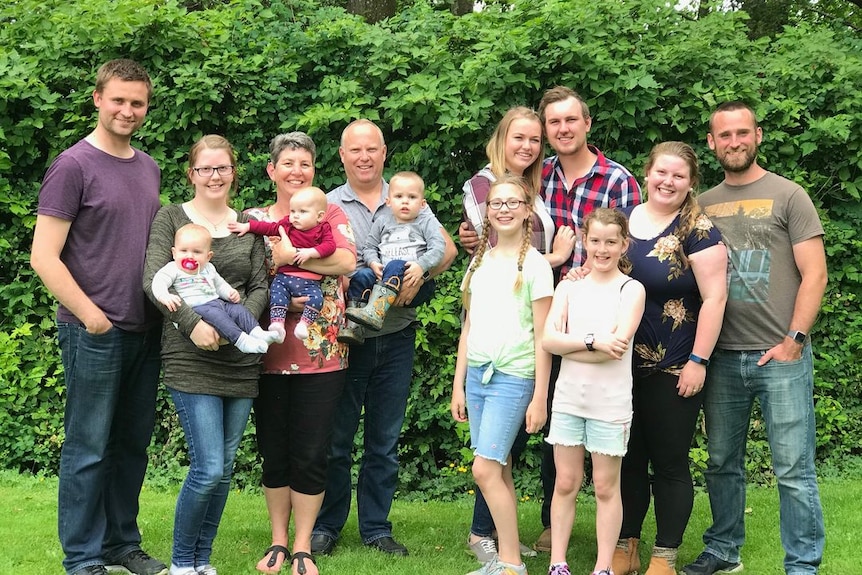 A family of adults and children pose for a photo in a leafy green setting