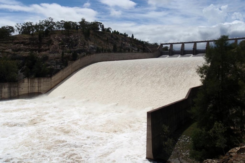 Water pours out of a dam from the top of a spillway down a slope