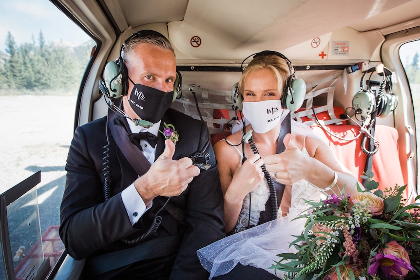Jeunes mariés dans des masques faciaux Covid avec les pouces vers le haut à l'intérieur d'un petit avion sur le point de décoller