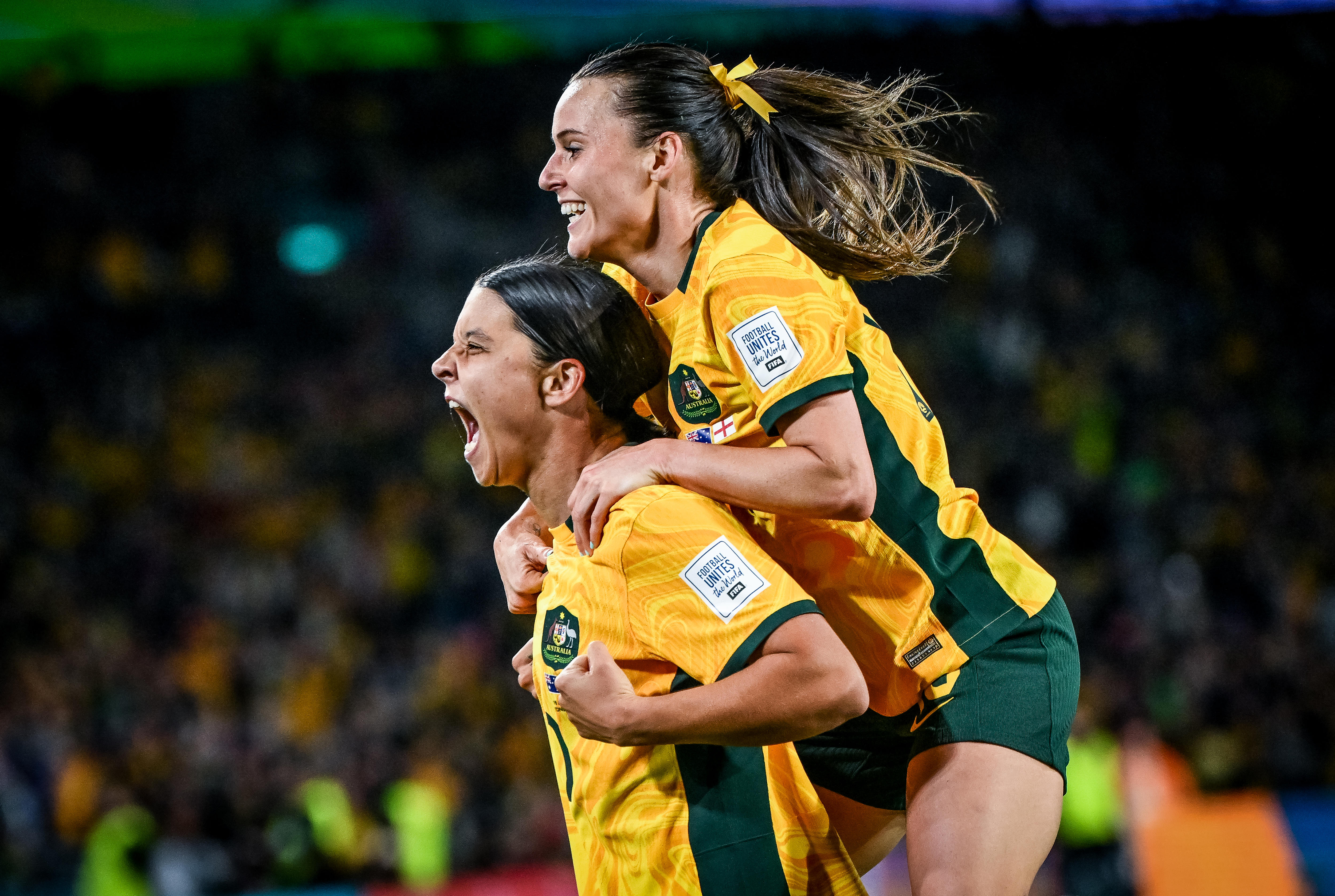 Side shot of a female soccer player yelling in joy with another player jumping on her back.