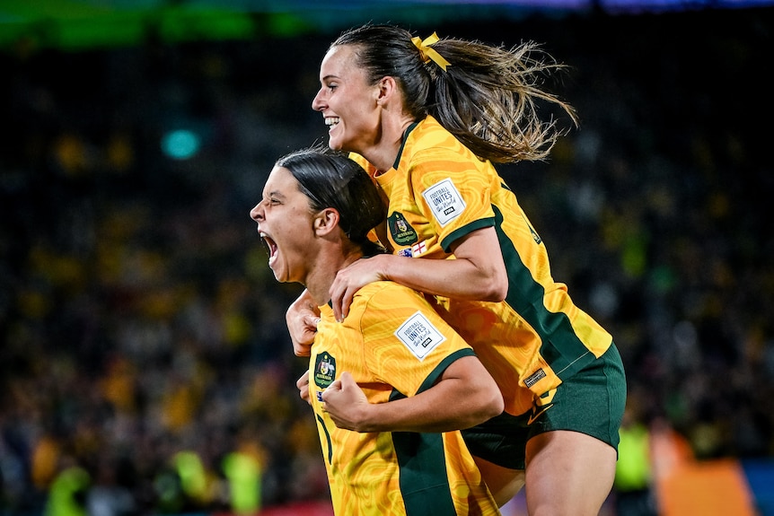 Side shot of a female soccer player yelling in joy with another player jumping on her back.