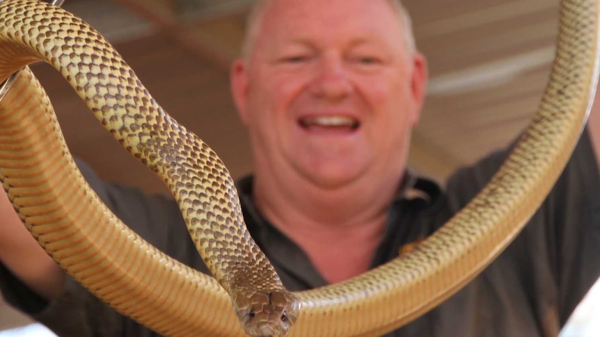 A smiling man holds a large snake.